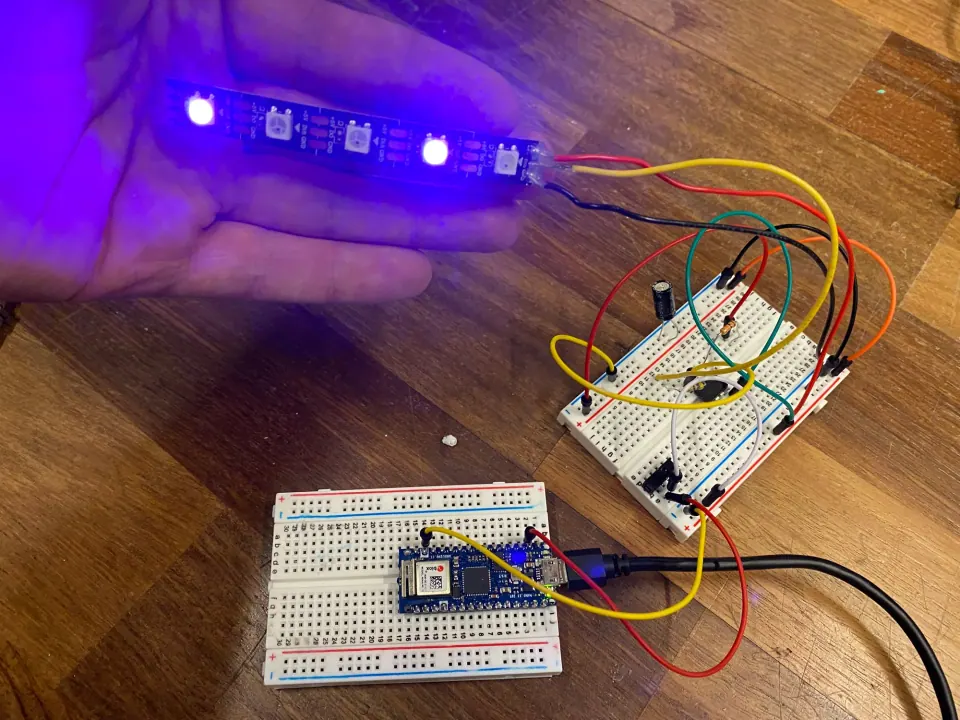NeoPixel LED strip held in a hand, glowing blue, wired to a breadboard and an Arduino Nano 33 IoT