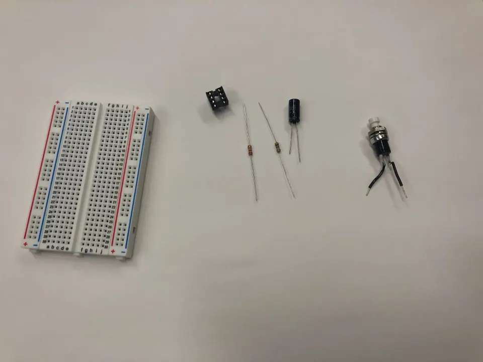 Breadboard, 8-pin chip socket, two resistors, a capacitor and a pushbutton laid out on a table
