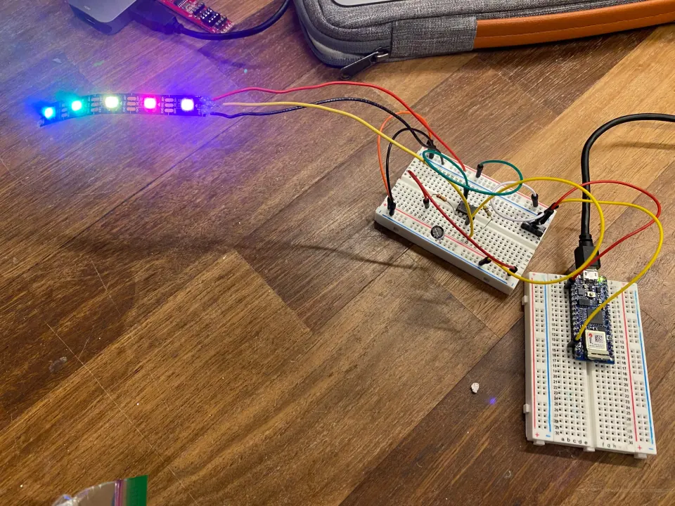 NeoPixel strip lit in several colours, wired to a breadboard and an Arduino Nano 33 IoT on a wooden floor