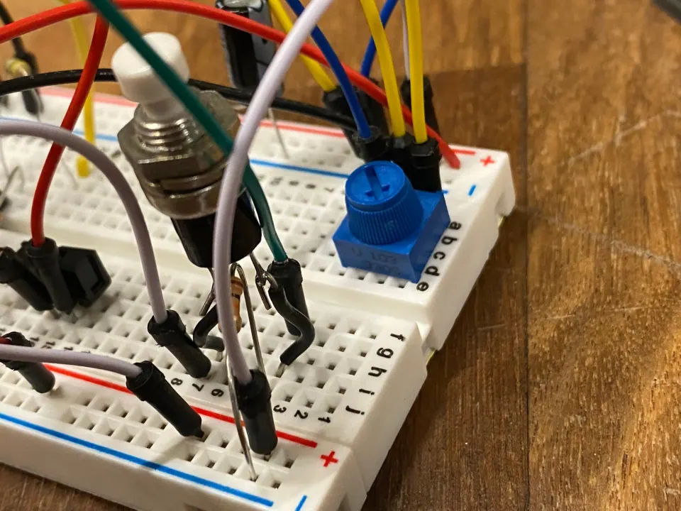 Close-up of a pushbutton and a blue trim pot on a breadboard with jumper wires