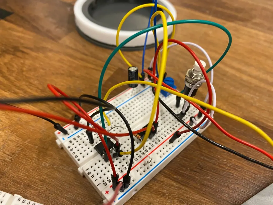 Breadboard prototype with a trim pot, capacitor and a tangle of jumper wires, next to the white ring of the enclosure