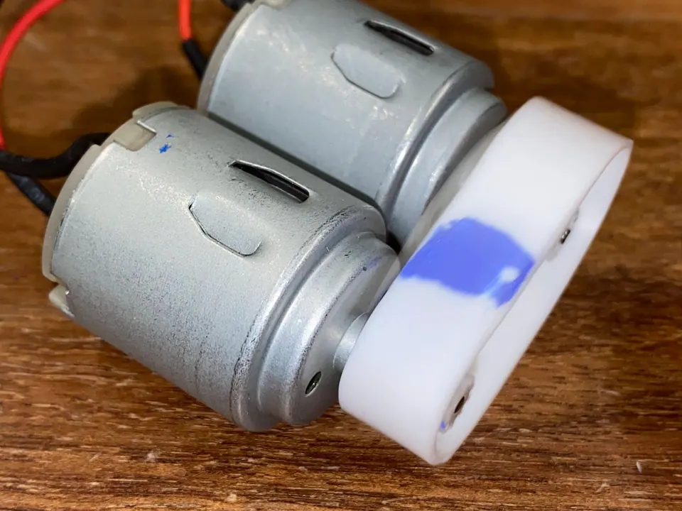 Two small silver DC motors beside a white 3D-printed wheel with a blue mark