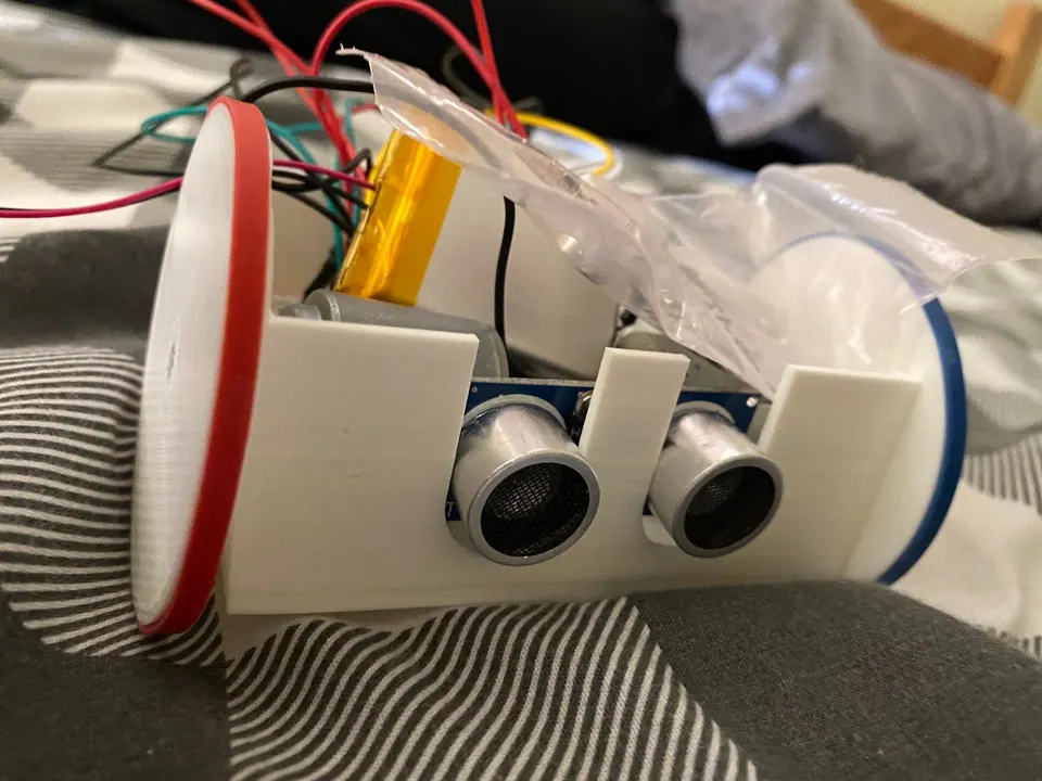 White 3D-printed robot body with two wheels, an ultrasonic distance sensor on the front and a yellow battery and wires inside