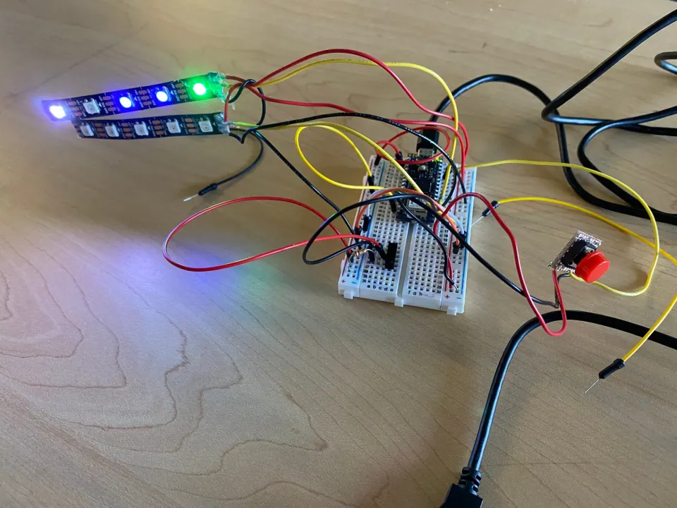 Two NeoPixel strips glowing blue and green, wired to an Arduino on a breadboard with a red pushbutton on long leads