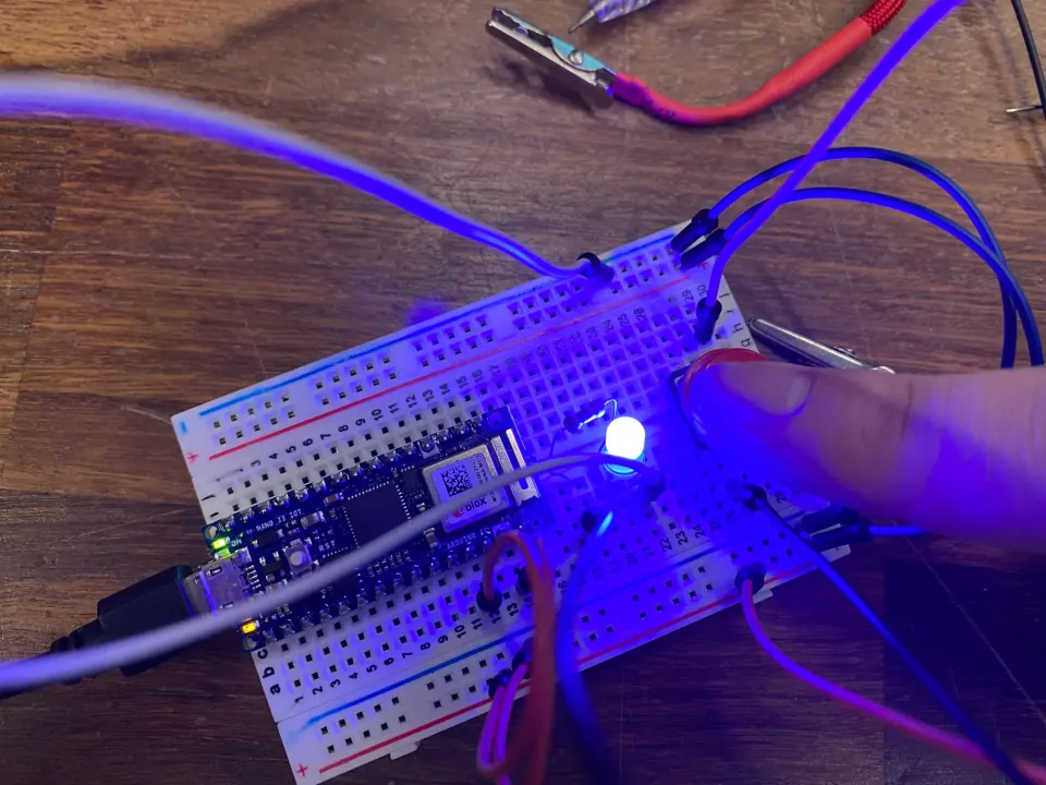 Breadboard with a blue LED lit and a fingertip pressing a button