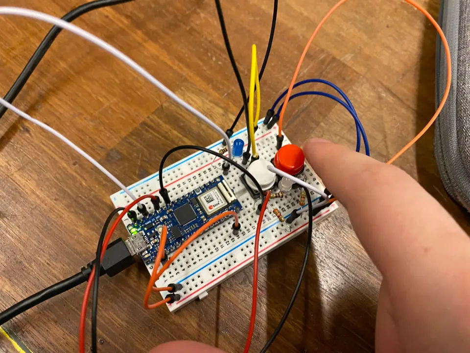 Breadboard circuit with a white and a red pushbutton and a blue LED, with a finger reaching for the buttons