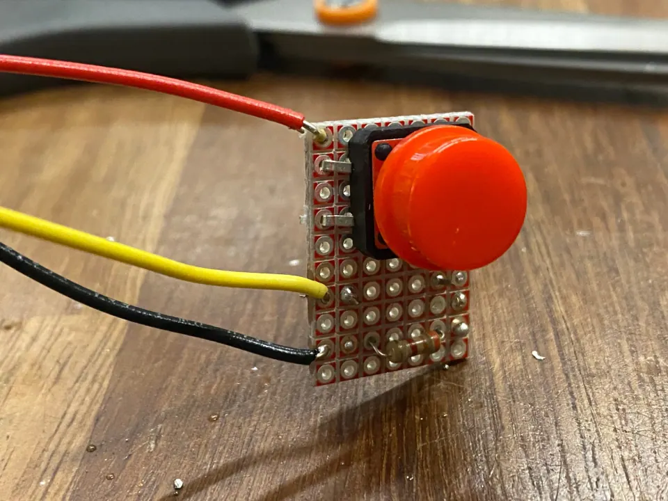 Protoboard with a red pushbutton soldered on and red, yellow and black wires attached