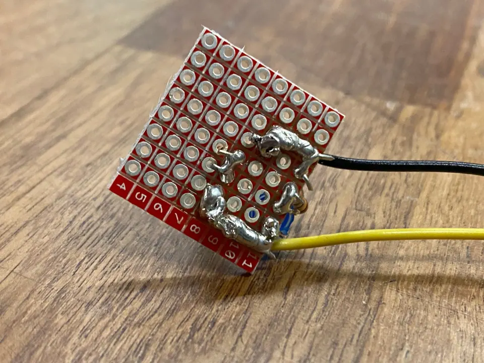 Underside of the LED protoboard with thick blobs of solder joining pads and black and yellow wires