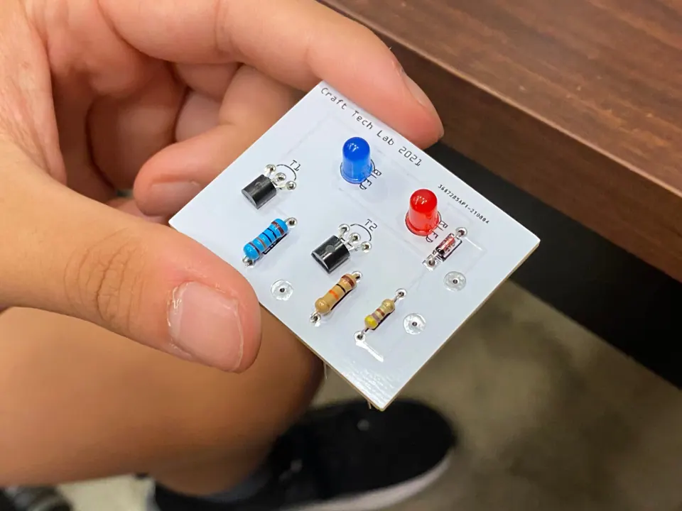Hand holding the white logic probe circuit board with a blue LED, a red LED, transistors and resistors fitted