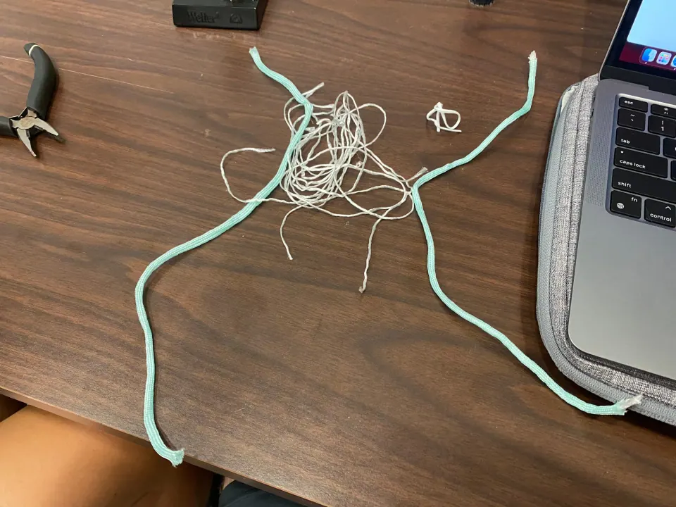 Two lengths of mint paracord and a tangle of white thread on a table beside a laptop
