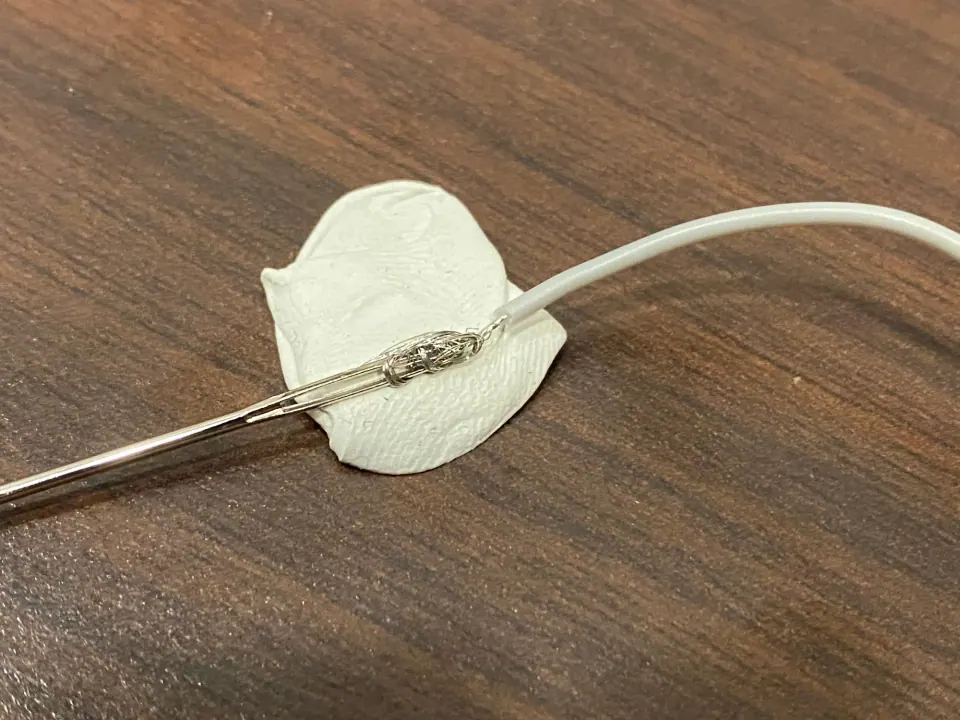 A thin wire soldered to the eye of a sewing needle on a piece of white fabric