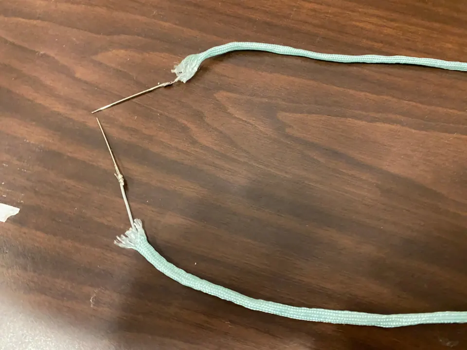 Two lengths of mint paracord with sewing needles attached at their frayed ends