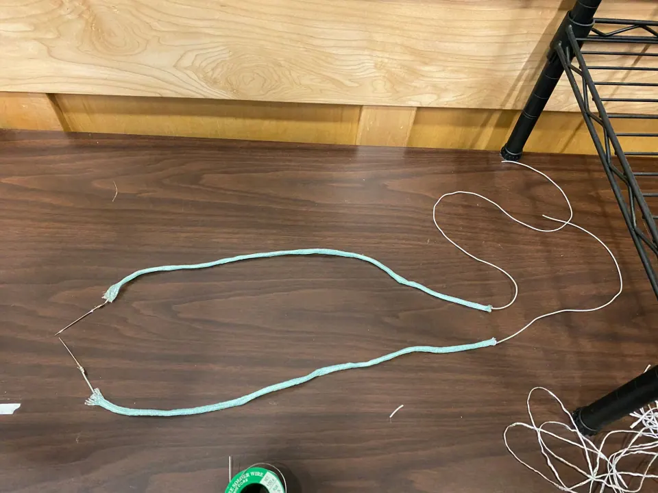 Two long mint paracord strands laid out on a table, with needles at one end and thin wire trailing from the other