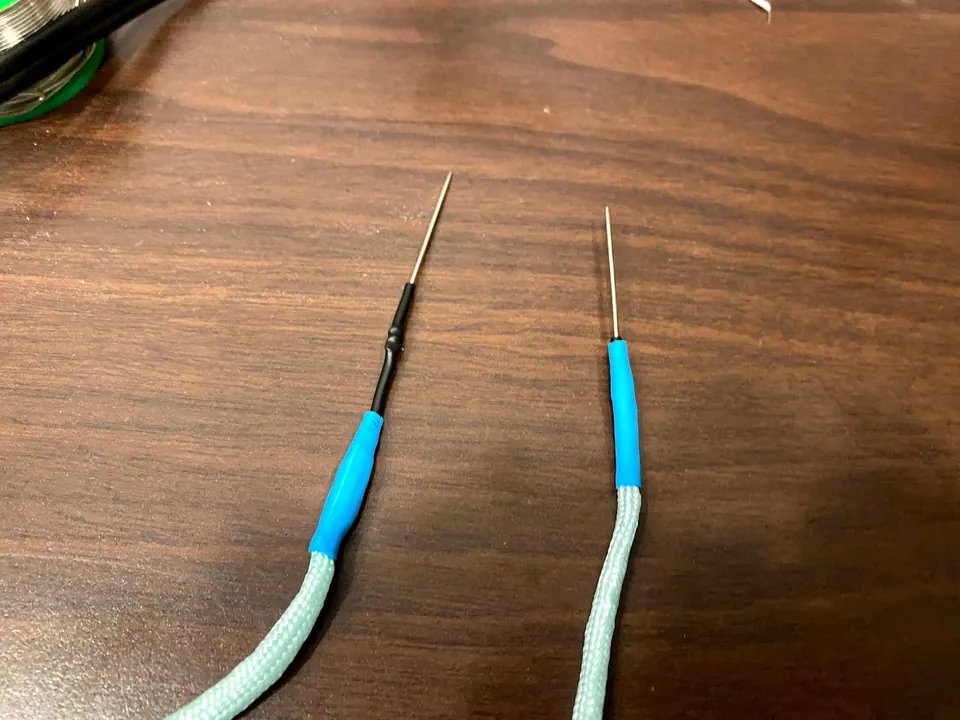 Two finished probe tips: sewing needles sticking out of paracord covered with blue heat shrink