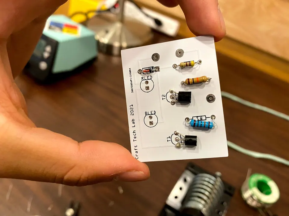 Hand holding the circuit board with resistors, transistors and a diode soldered in and the LED positions empty