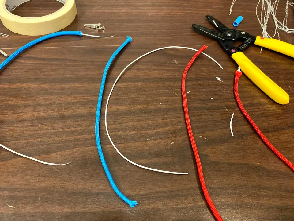 Blue, red and white wires cut to length beside wire strippers and masking tape