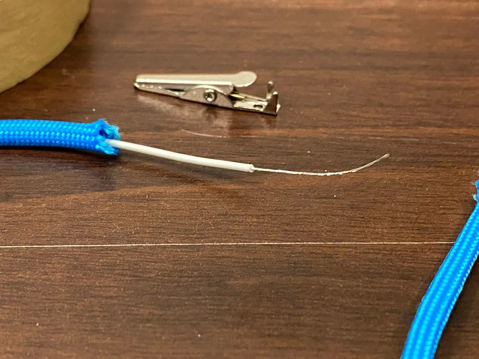 A blue paracord end with stripped white wire, next to an alligator clip