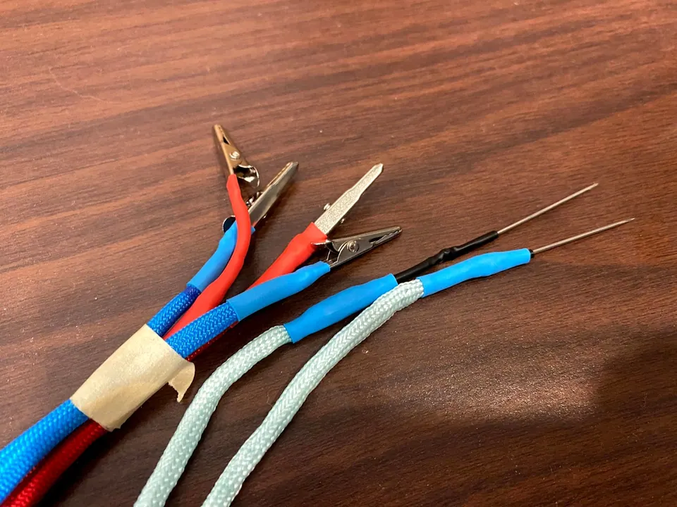 Close-up of the cable ends: alligator clips on the blue and red cords and needle probes on the mint cords, finished with blue heat shrink