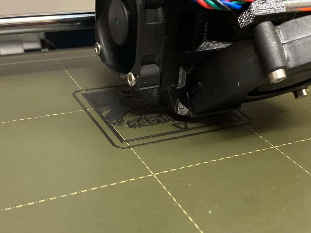 Printer nozzle over a print in progress on the bed, with the lettering visibly distorted
