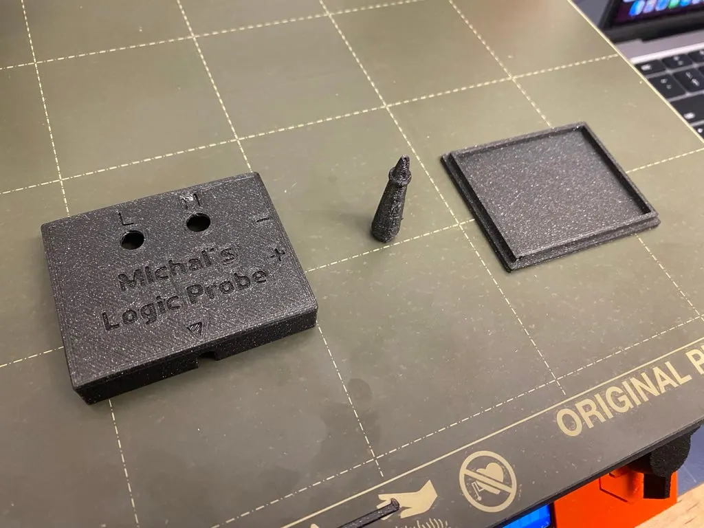 Printed housing top, a small cone-shaped part and the shallow lid lying on the Prusa print bed