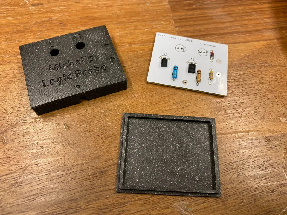 Black printed housing top and lid beside the assembled circuit board on a wooden table