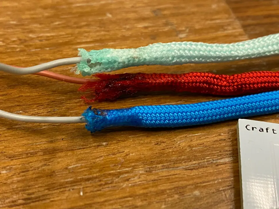 Ends of mint, red and blue paracord with melted, fraying fibres and grey wire coming out