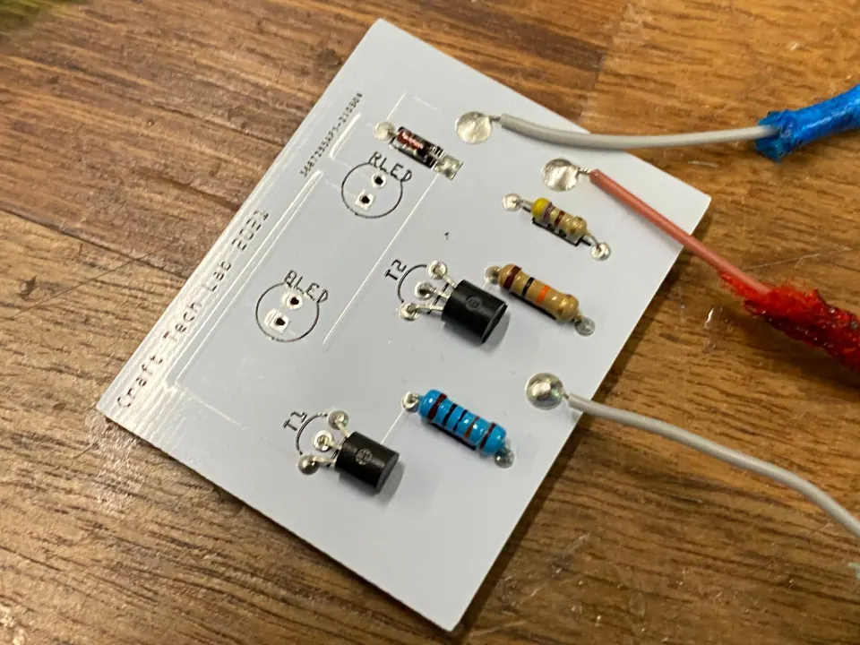 Circuit board with grey and pink wires soldered through the board and blue and red cords attached