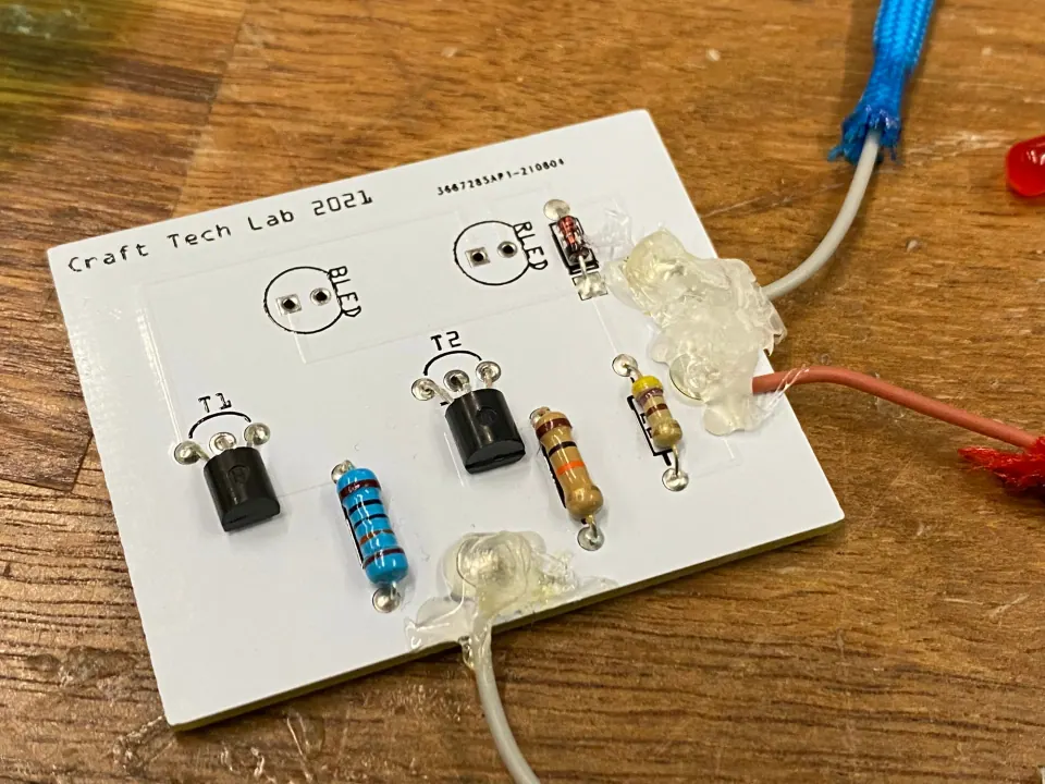 Circuit board with a large lump of hot glue holding the wires, and a loose red LED beside it