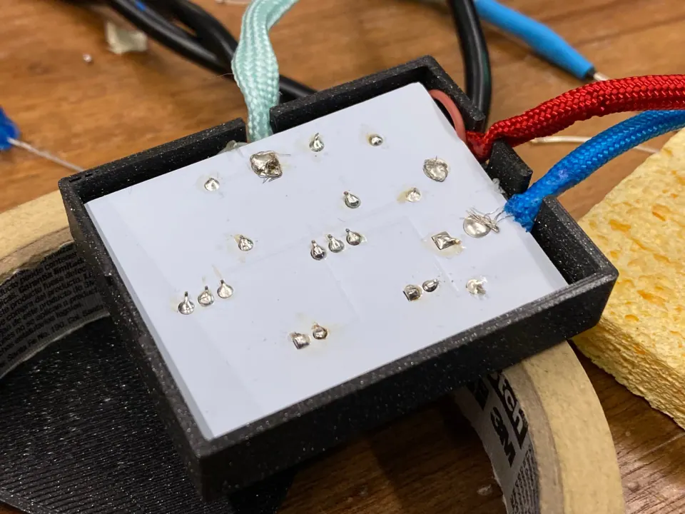 Underside of the circuit board seated in the black housing, showing solder joints, with red and blue cords exiting