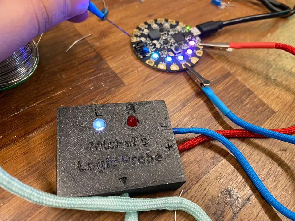 Needle probe touching the Circuit Playground board with the white L LED lit