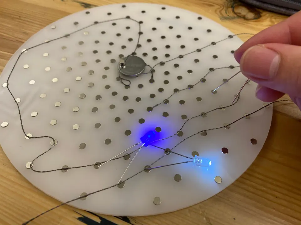 ThreadBoard with the blue and white LEDs lit and a fingertip touching a thread end