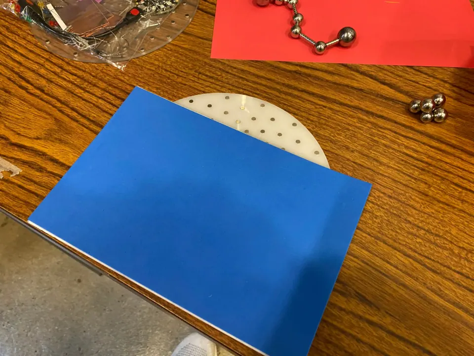 Sheet of blue foam laid over the ThreadBoard on a table, with a ball chain on red paper nearby