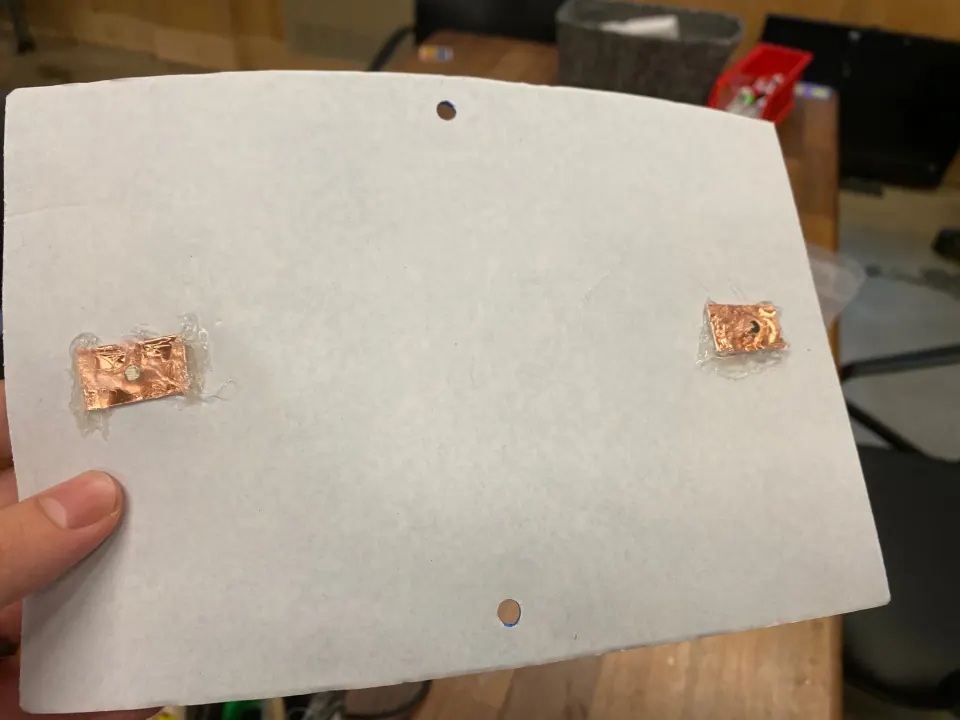 Foam sheet held up, with two copper pads hot-glued to its white back