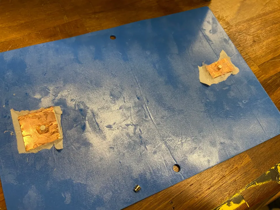 Back of the blue foam with the white backing ripped away and two copper pads taped on, each with a magnet