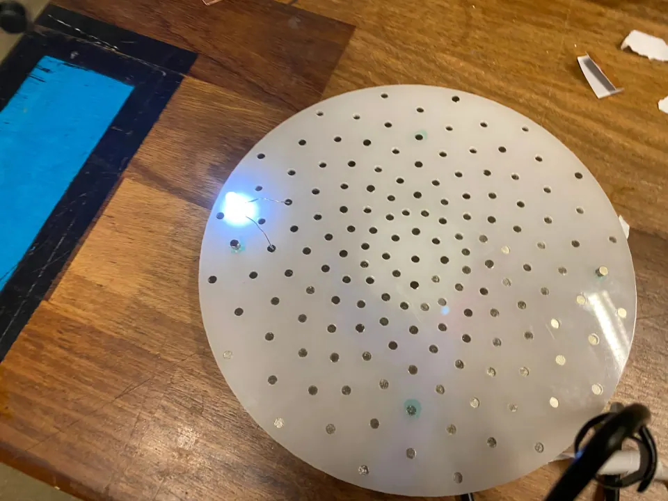 Underside of the ThreadBoard disc with one blue-white LED lit at the left edge