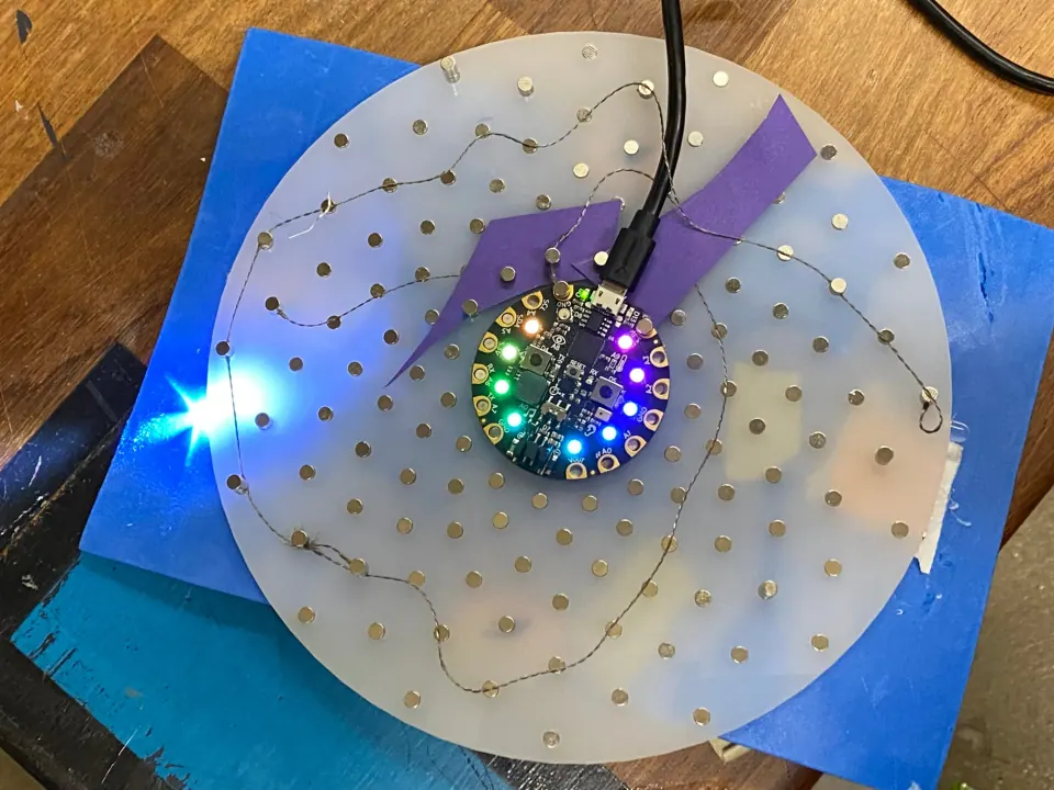 Finished ThreadBoard from above, with the Circuit Playground board in the middle, a bright white LED at the left edge and blue foam beneath