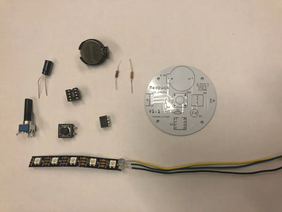 Components laid out beside the PCB: a capacitor, a trim pot, an 8-pin socket and chip, a pushbutton, a coin cell, two resistors and a NeoPixel strip with wires