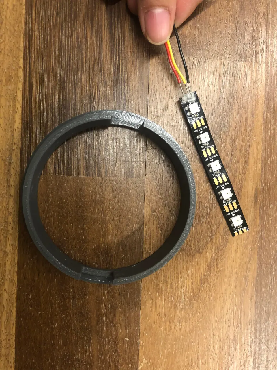 Hand holding the NeoPixel strip next to the grey 3D-printed ring