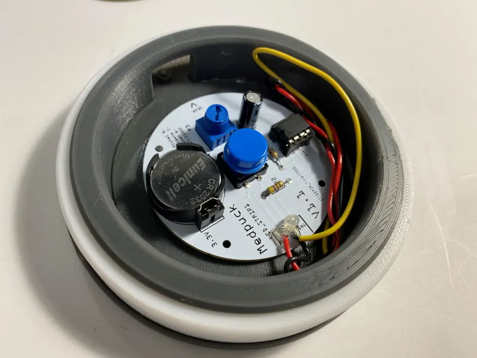 Top view of the assembled MedPuck with PCB, coin cell, blue trim pot and pushbutton inside the grey ring and white outer shell