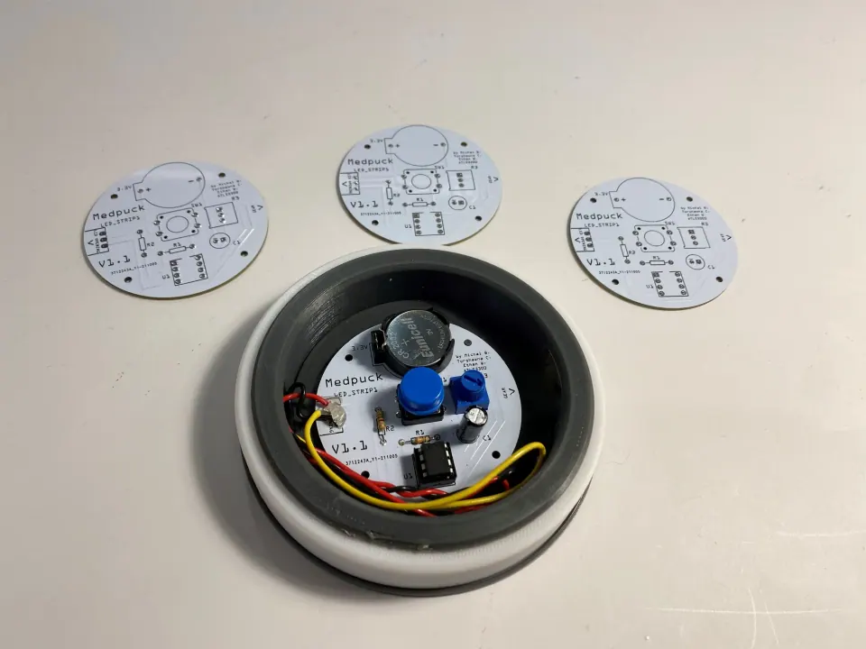 Assembled MedPuck prototype surrounded by three bare MedPuck PCBs