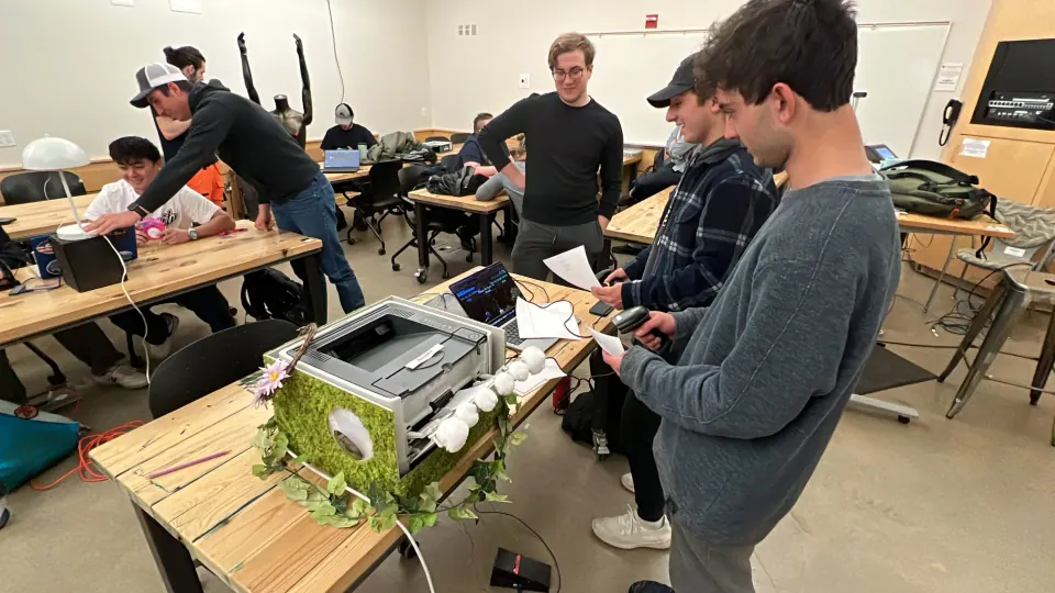 Students playtesting around the mossy printer enclosure in a classroom