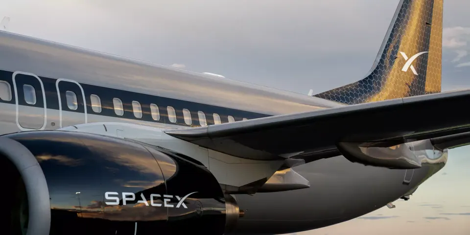 Close-up of a black and gold jet wing and engine with SpaceX branding, lit at dusk