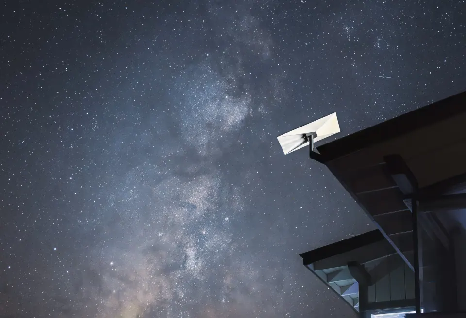 A Starlink dish on the corner of a roof under a night sky full of stars and the Milky Way